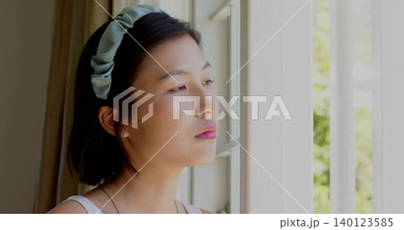 Gazing Korean woman by window at home, wearing pale tank top, pale-green padded headband, necklace Gazing Korean woman by window at home, wearing pale tank top, pale-green padded headband, necklace 140123585