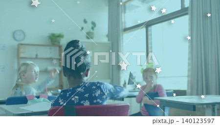 Sitting child with bun wearing dark blue floral top in classroom, blue folder and star stickers Sitting child with bun wearing dark blue floral top in classroom, blue folder and star stickers 140123597