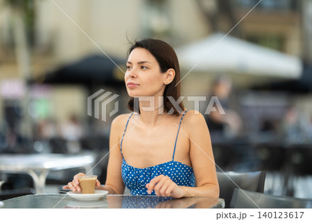 Smiling stylish brunette woman drinking espresso coffee while sitting on terrace of street cafe Smiling stylish brunette woman drinking espresso coffee while sitting on terrace of street cafe 140123617