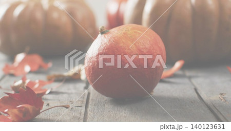 Displaying small orange pumpkin sitting on weathered wooden planks, with scattered autumn leaves Displaying small orange pumpkin sitting on weathered wooden planks, with scattered autumn leaves 140123631