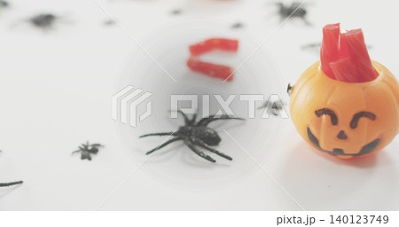 Sitting jack-o'-lantern on white table, holding red gummy strips with black spiders, copy space 140123749