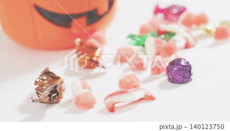 Showing Halloween candy cluster on white table, with pink gumdrops, foil chocolates, blurred bucket Showing Halloween candy cluster on white table, with pink gumdrops, foil chocolates, blurred bucket 140123750