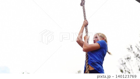 Climbing athletic woman pulling up on thick rope at outdoor fitness course, blue top, copy space Climbing athletic woman pulling up on thick rope at outdoor fitness course, blue top, copy space 140123769