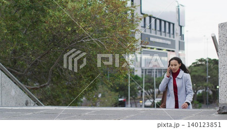 Walking woman ascending plaza steps, on phone, wearing gray coat red sweater, brown bag, copy space 140123851