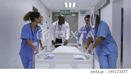 Pushing medical staff in scrubs and coat guiding covered gurney through ward, holding IV pole Pushing medical staff in scrubs and coat guiding covered gurney through ward, holding IV pole 140123877