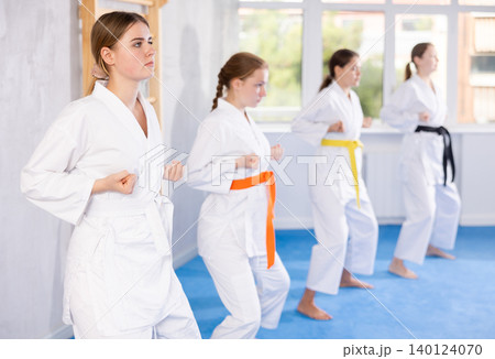 Team of teenage girls in kimonos stand in fighting stance during group karate training session Team of teenage girls in kimonos stand in fighting stance during group karate training session 140124070