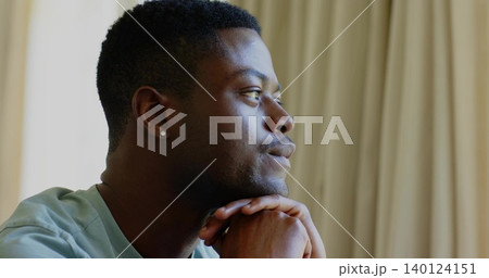 Gazing man wearing green tee, resting chin on hands at home, stud earring, curtains, copy space 140124151