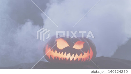 Glowing carved jack-o'-lantern casting warm orange light on flat dark surface, surrounded by smoke 140124250