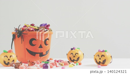 Displaying orange pumpkin bucket holding wrapped candies on white tabletop with spider, copy space 140124321