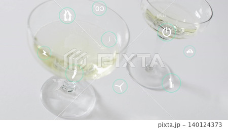 Displaying two coupe glasses holding pale yellow liquid on white tabletop, with teal UI icons Displaying two coupe glasses holding pale yellow liquid on white tabletop, with teal UI icons 140124373