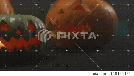 Glowing two carved jack-o'-lanterns casting orange reflections on studio tabletop, calibration grid 140124374