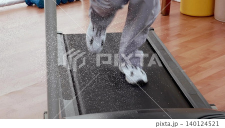 Running child wearing grey sweatpants and white shoes on home treadmill, kicking up dust Running child wearing grey sweatpants and white shoes on home treadmill, kicking up dust 140124521