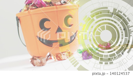 Overflowing orange jack-o'-lantern bucket spilling foil candies on white table, with green overlay Overflowing orange jack-o'-lantern bucket spilling foil candies on white table, with green overlay 140124537