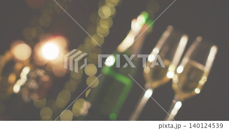 Showing green champagne bottle and three stemmed flutes resting on party tabletop with fairy lights Showing green champagne bottle and three stemmed flutes resting on party tabletop with fairy lights 140124539