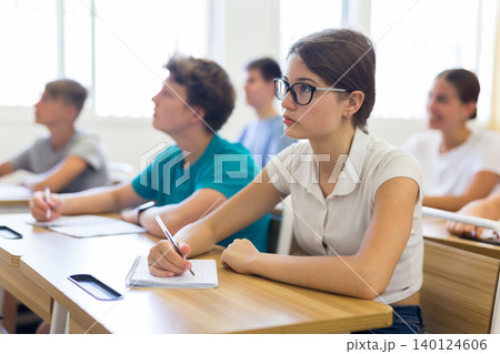 High school student teenage girl studying in college with classmates, making notes of teacher lecture High school student teenage girl studying in college with classmates, making notes of teacher lecture 140124606