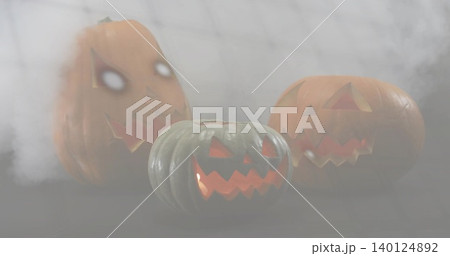 Displaying carved gray-green pumpkin glowing on dark table with two lit orange pumpkins and fog Displaying carved gray-green pumpkin glowing on dark table with two lit orange pumpkins and fog 140124892
