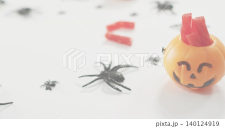 Showing orange pumpkin bucket holding red candy sticks on white desk with black spiders, copy space Showing orange pumpkin bucket holding red candy sticks on white desk with black spiders, copy space 140124919