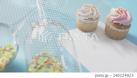 Showing two sprinkled cupcakes on pastel-blue table, inverted glasses, dotted light, copy space Showing two sprinkled cupcakes on pastel-blue table, inverted glasses, dotted light, copy space 140124923