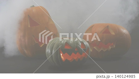 Glowing three carved pumpkins emitting warm inner light on dark tabletop with drifting smoke Glowing three carved pumpkins emitting warm inner light on dark tabletop with drifting smoke 140124985