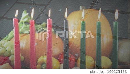 Flickering row of red black green tapered candles glowing on kitchen table with pumpkin, grapes 140125188