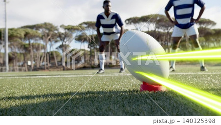 Balancing white rugby ball on red tee on grass pitch, neon streaks, players wearing striped jerseys Balancing white rugby ball on red tee on grass pitch, neon streaks, players wearing striped jerseys 140125398