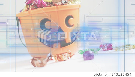 Sitting orange jack-o-lantern bucket holding foil candies on white tabletop, with digital overlays Sitting orange jack-o-lantern bucket holding foil candies on white tabletop, with digital overlays 140125454