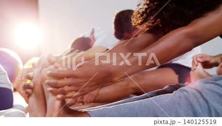 Reaching curly woman stretching on gym mats with ball, sportswear, bare toes, light flare 140125519