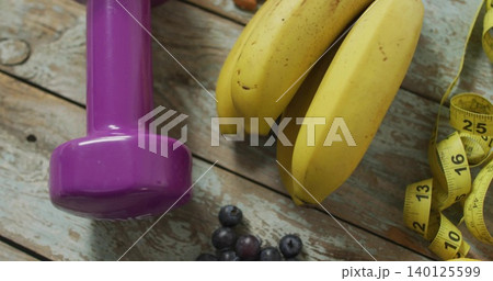 Displaying purple dumbbell with ripe bananas on wood plank, showing yellow tape and blueberries Displaying purple dumbbell with ripe bananas on wood plank, showing yellow tape and blueberries 140125599