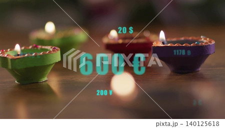Flickering painted diyas showing flames on polished wood table, circular bokeh, turquoise overlays 140125618