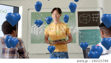 Presenting pupil wearing yellow tee, jeans holding tablet in class with periodic table, blue hearts Presenting pupil wearing yellow tee, jeans holding tablet in class with periodic table, blue hearts 140125789
