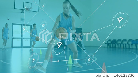 Dribbling player in blue jersey navigating cones in school gym, with balls, hoop, network overlay 140125830