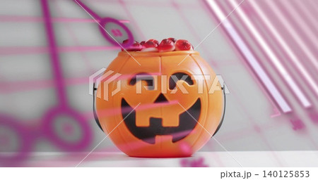 Sitting orange jack-o'-lantern bucket holding red gummies on white tabletop, pink reflections Sitting orange jack-o'-lantern bucket holding red gummies on white tabletop, pink reflections 140125853