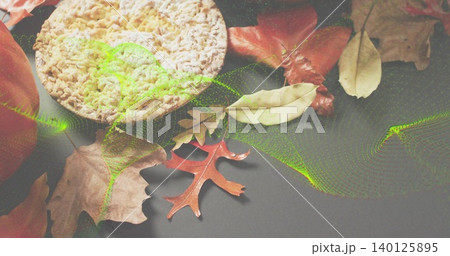 Resting rice cake on dark table among dried leaves, oak leaf, partial apple, neon green overlay 140125895