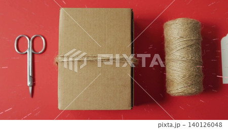 Displaying brown box wrapped with jute twine on red craft table with scissors, spool, tag 140126048