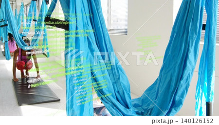 Kneeling woman in pink top, shorts practicing pose at fitness studio with blue silks, green code Kneeling woman in pink top, shorts practicing pose at fitness studio with blue silks, green code 140126152