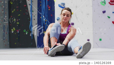 Adjusting woman tying shoe strap on padded floor, colorful holds and ropes, wearing purple tank top Adjusting woman tying shoe strap on padded floor, colorful holds and ropes, wearing purple tank top 140126169