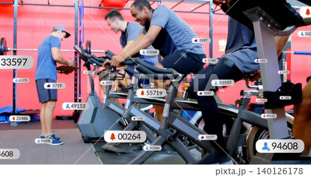 Pedaling man wearing navy t-shirt and dark shorts on spin bike at fitness studio, with badges 140126178
