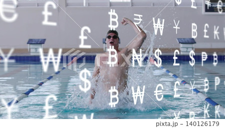 Emerging male swimmer raising right fist in lap pool, wearing goggles and trunks, currency overlay Emerging male swimmer raising right fist in lap pool, wearing goggles and trunks, currency overlay 140126179