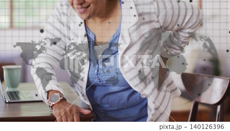 Leaning senior Indian woman supporting back at home in cardigan with laptop and map overlay Leaning senior Indian woman supporting back at home in cardigan with laptop and map overlay 140126396