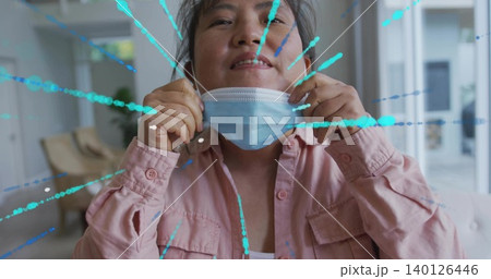 Grasping ear loops, Korean man pulling blue mask beneath chin in lobby, pink shirt, teal splatter 140126446