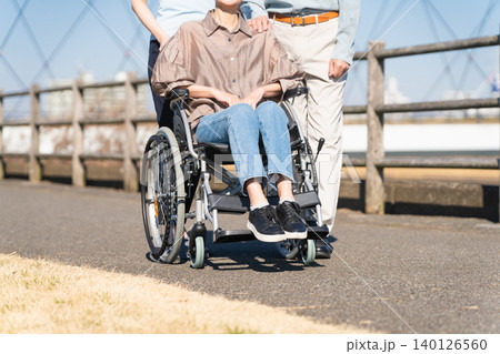 車椅子を押して散策する熟年夫婦と介護士 車椅子を押して散策する熟年夫婦と介護士 140126560