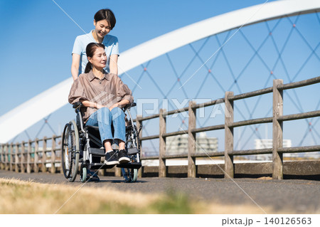 車椅子を押して散策する女性と介護士 車椅子を押して散策する女性と介護士 140126563