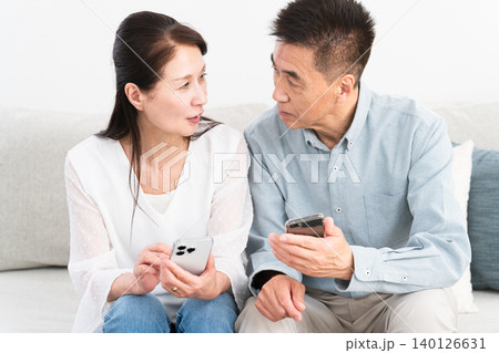 ソファーに座ってスマートフォンを操作している熟年夫婦 ライフスタイルイメージ ソファーに座ってスマートフォンを操作している熟年夫婦 ライフスタイルイメージ 140126631