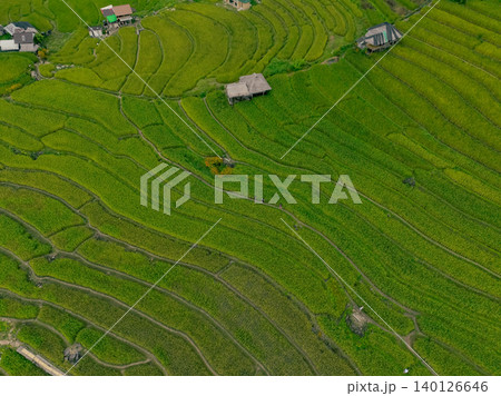Aerial view of lush green rice terraces in mountain with patterns and small rural homes. Sustainable farming and eco tourism in Asia. Organic agriculture and homestays promoting rural development. Aerial view of lush green rice terraces in mountain with patterns and small rural homes. Sustainable farming and eco tourism in Asia. Organic agriculture and homestays promoting rural development. 140126646