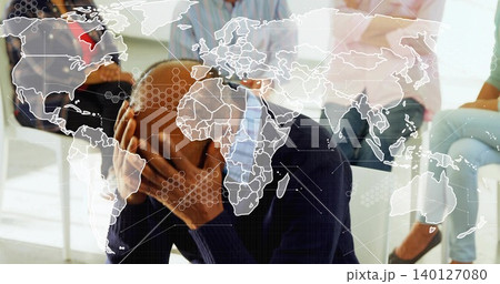 Hunching bald man in business-casual covering face at support group, white chairs, map overlay 140127080