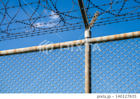 Barbed wire fence symbolizing border control, geopolitical tensions, and restricted freedoms in modern society. Barbed wire border security fence. Barrier border. Boundary security wall. Private area. Barbed wire fence symbolizing border control, geopolitical tensions, and restricted freedoms in modern society. Barbed wire border security fence. Barrier border. Boundary security wall. Private area. 140127635