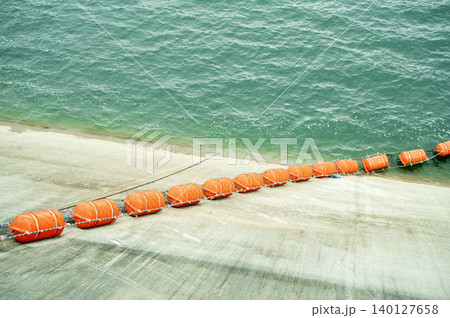 Line of orange debris barrier floating near intake zone of a hydroelectric dam to protect turbine system from vegetation and log blockage during active power generation and water flow control. Line of orange debris barrier floating near intake zone of a hydroelectric dam to protect turbine system from vegetation and log blockage during active power generation and water flow control. 140127658