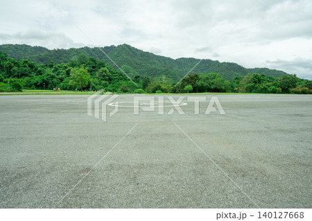 Empty helicopter landing pad with asphalt with green mountain forest background providing emergency medical transport access to remote wilderness areas. Helipad platform at dam infrastructure site. Empty helicopter landing pad with asphalt with green mountain forest background providing emergency medical transport access to remote wilderness areas. Helipad platform at dam infrastructure site. 140127668
