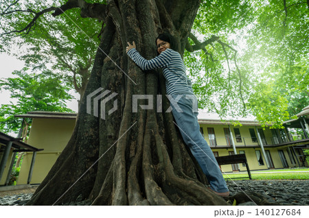 Asian woman hugging big tree trunk. Eco retreat. Nature connection therapy for mental health wellness and digital detox healing in natural environment. Mental wellness and digital detox at eco hotel. 140127684