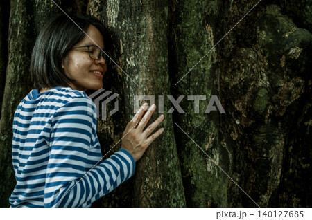 Woman practicing forest therapy mindfulness meditation leaning face against tree trunk. Digital detox retreat. Spiritual healing and natural wellness. Reconnecting with nature. Forest bathing therapy. Woman practicing forest therapy mindfulness meditation leaning face against tree trunk. Digital detox retreat. Spiritual healing and natural wellness. Reconnecting with nature. Forest bathing therapy. 140127685